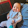 baby, infant, pacifier, onesie, bib, couch, pillow, quilt, star_pattern, child, indoor, relaxed, plush, smiling, cute, comfortable, clothing, person, portrait, home