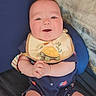 baby, infant, bib, turtle, clothing, smile, hands, sitting, cushion, blue_background, usa_flag, pattern, happy, cute, portrait, child, indoor, rosy_cheeks, shorts, onesie