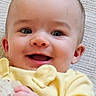 baby, blanket, child, close_up, couch, ears, eyes, face, fluffy, hand, happy, indoor, infant, long_sleeves, photograph, portrait, smartphone_screenshot, smiling, textile, yellow_clothing