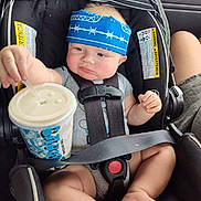 Louie is registered to the contest to win money with this photo: baby, car_seat, bandana, drink, straw, clothing, seat_belt, child, infant, car_interior, person, cute, expression, hand, foot, headwear, sitting, safety_harness, drink_cup, pout