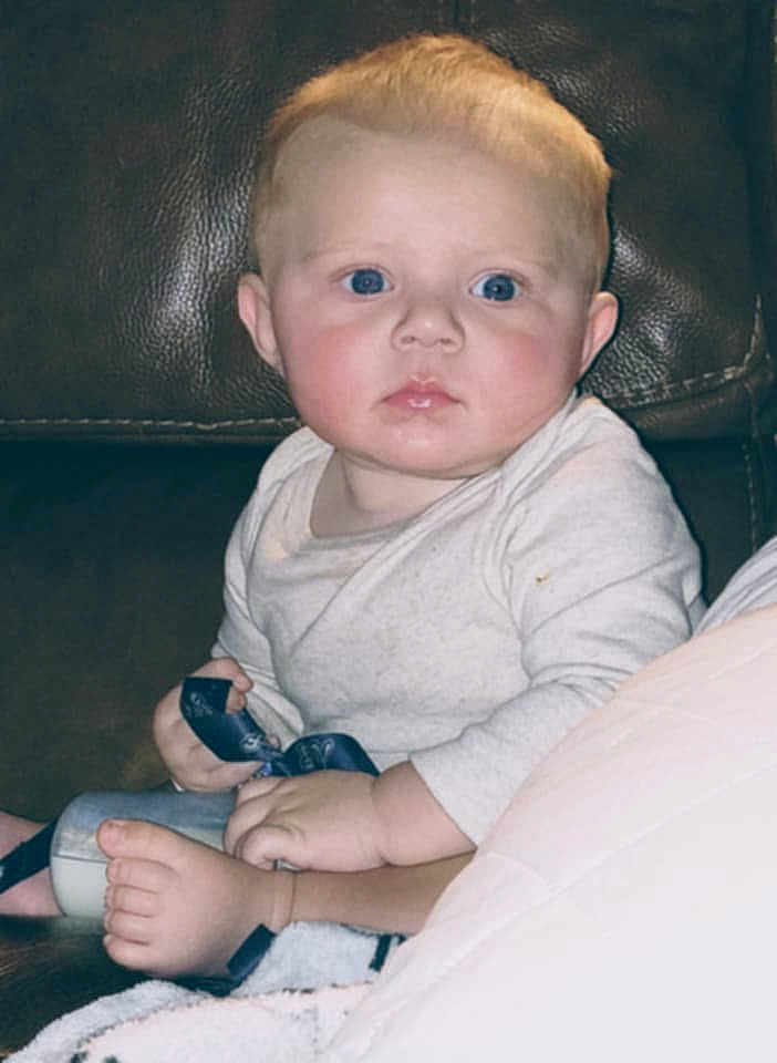 Louie joined the competition — help win amazing prizes! baby, infant, child, blue_eyes, sitting, clothing, foot, hand, leather_couch, indoor, curious, cute, portrait, young_child, skin, face, person, home, casual, expression