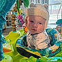 Louie joined the competition — help win amazing prizes! baby, child, hat, plush_hat, activity_center, toy, indoor, window, curtains, blue_onesie, dinosaur_print, face, person, play, colorful, green, pink_toy, soft_lighting, floor, home