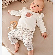 Talia a rejoint le concours — aidez-le/la à gagner de superbes lots ! baby, infant, child, lying_down, cushion, toy, wooden_toy, clothing, white_clothes, patterned_pants, deer_design, soft_texture, indoors, cute, gazing_up, barefoot, pink_cheeks, comfortable, relaxed, nursery