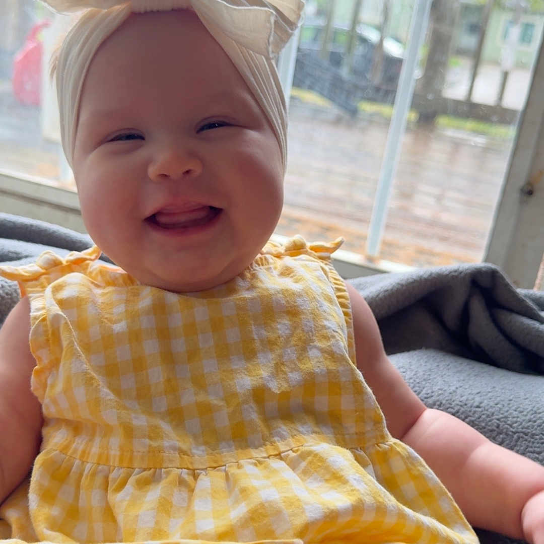 Lila joined the competition — help win amazing prizes! baby, baby_dress, child, chubby_cheeks, closeup, clothing, cute, face, happy, headband, headwear, indoors, infant, natural_light, person, portrait, sitting, smiling, window, yellow_dress