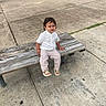 Bryant is registered to the contest to win money with this photo: child, bench, outdoor, pavement, grass, person, white_shirt, striped_pants, sandals, curly_hair, expression, wood, park, sidewalk, concrete, casual_clothing, seated, daylight, urban, young_child