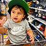 Bryant is registered to the contest to win money with this photo: toddler, child, shopping_cart, green_cap, nike_shirt, store, aisle, hats, clothing, shelves, retail, brown_shorts, curly_hair, expression, gesture, indoor, person, young_child, casual_wear, shopping
