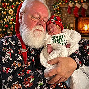 Aaron is registered to the contest to win money with this photo: baby, christmas, santa_claus, sleeping, holiday, festive, beard, glasses, red_hat, blanket, fireplace, stockings, tree, decorations, warmth, indoors, cozy, holding, face, person