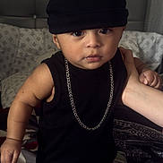 Rodrigo is registered to the contest to win money with this photo: baby, child, toddler, portrait, standing, bed, bedroom, beanie, black_clothing, gold_chain, camouflage_pants, fashion, cute, serious_expression, brown_eyes, indoor, adult_hand, bedding, headboard, photography