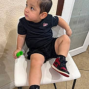 Anders Corria joined the competition — help win amazing prizes! child, toddler, portrait, sitting, chair, black_shirt, black_shorts, sneakers, red_shoes, green_object, fashion, casual_clothing, indoors, wall, door, window, tile_floor, looking_away, single_person, full_body