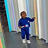 toddler, child, blue_clothing, hoodie, sneakers, toy, light_up_toy, indoor, modern, colorful, panels, floor, smiling, happy, standing, person, playful, young_child, casual_wear, bright