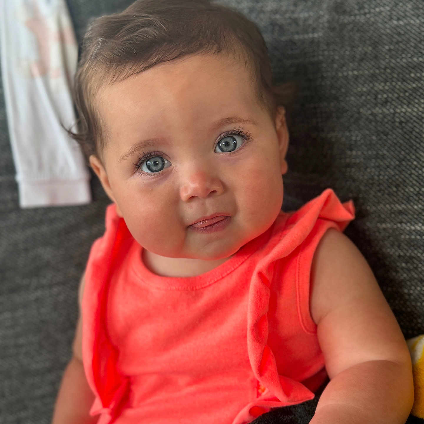 Amelia joined the competition — help win amazing prizes! baby, blanket, blue_eyes, child, closeup, coral_clothing, couch, curly_hair, cute, face, happy, home, indoor, infant, person, portrait, sitting, smiling, soft_light, young_child