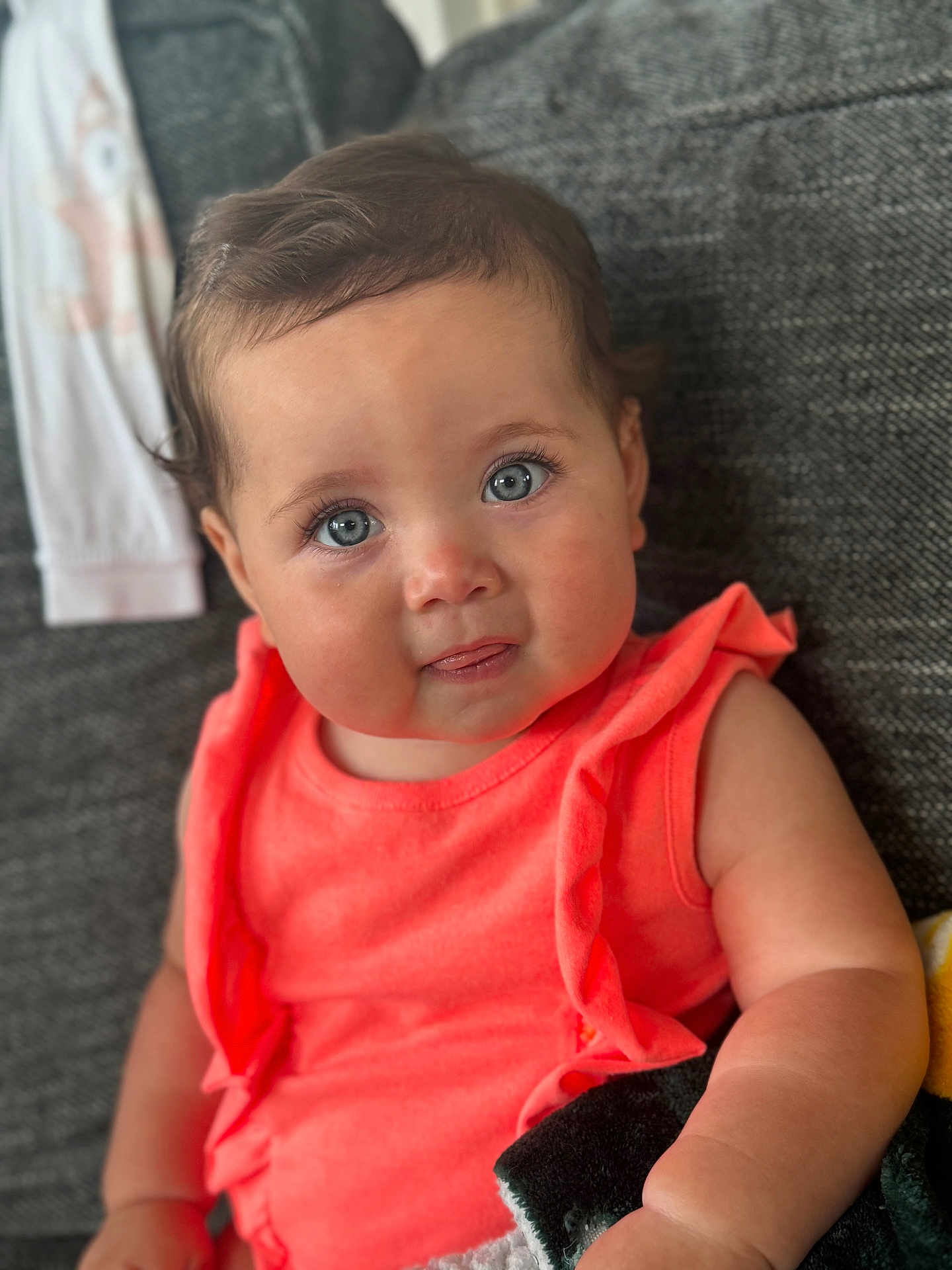 Amelia joined the competition — help win amazing prizes! baby, child, blue_eyes, coral_clothing, couch, blanket, indoor, face, curly_hair, cute, infant, portrait, smiling, sitting, soft_light, person, home, closeup, happy, young_child