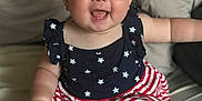 Amelia is registered to the contest to win money with this photo: baby, child, smiling, happy, blue_eyes, dress, stars, stripes, sitting, bed, indoor, cute, infant, person, skin, chubby, hand, foot, portrait, clothing