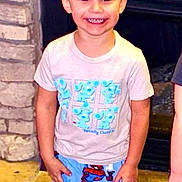 Kholton is registered to the contest to win money with this photo: child, boy, smiling, standing, indoor, tshirt, pajamas, spiderman, cartoon, face, happy, short_hair, stone_wall, fireplace, floor, person, clothing, casual, cute, young