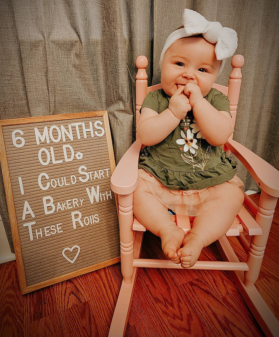 Cassidy is registered to the contest to win money with this photo: arm, baby, baby_toddler_clothing, chair, finger, flash_photography, hand, happy, headwear, human_body, human_leg, joint, knee, leg, pattern, person, pink, skin, sleeve, thigh