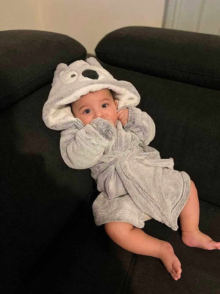Klei participe au concours pour gagner de l'argent avec cette photo : baby, child, infant, bathrobe, hood, animal_hood, grey, couch, sofa, black, indoor, cute, cozy, relaxed, person, face, eyes, legs, barefoot, furniture