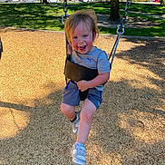 Dominic joined the competition — help win amazing prizes! child, toddler, swing, playground, outdoor, sunny, wood_chips, tree, grass, smiling, happy, casual_clothing, shorts, tshirt, sneakers, metal_chain, daytime, park, person, recreation