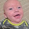 John joined the competition — help win amazing prizes! baby, infant, smiling, face, blue_eyes, camo_clothing, onesie, happy, cute, skin, head, portrait, lying_down, closeup, newborn, child, young, human, indoors, casual