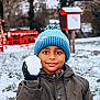 child, boy, snowball, winter, beanie, hat, glove, coat, jacket, smile, face, eyes, portrait, outdoors, park, snow, trees, playground_equipment, red_structure, candid