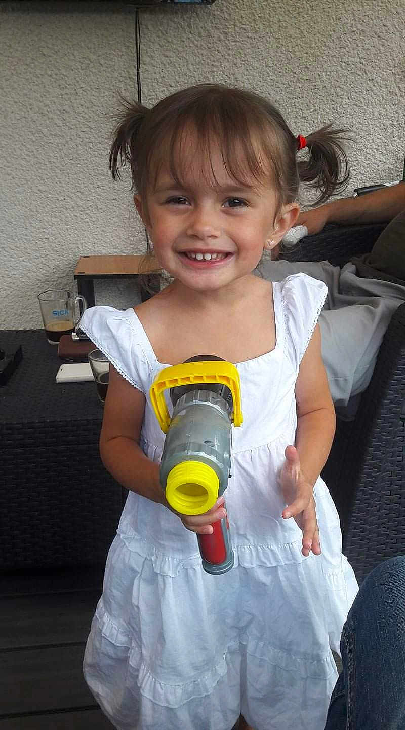 Lena a rejoint le concours — aidez-le/la à gagner de superbes lots ! child, girl, smiling, toy_gun, white_dress, pigtails, outdoor, patio, furniture, coffee_cup, person, happy, casual, hair, play, young, cute, portrait, daylight, relaxed