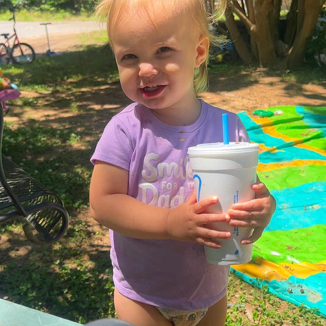 Louise joined the competition — help win amazing prizes! barefoot, bicycle, blonde_hair, blue_straw, child, daytime, diaper, grass, happy, nature, outdoor, pigtails, plastic_cup, play_mat, purple_shirt, smiling, summer, sunlight, toddler, tree