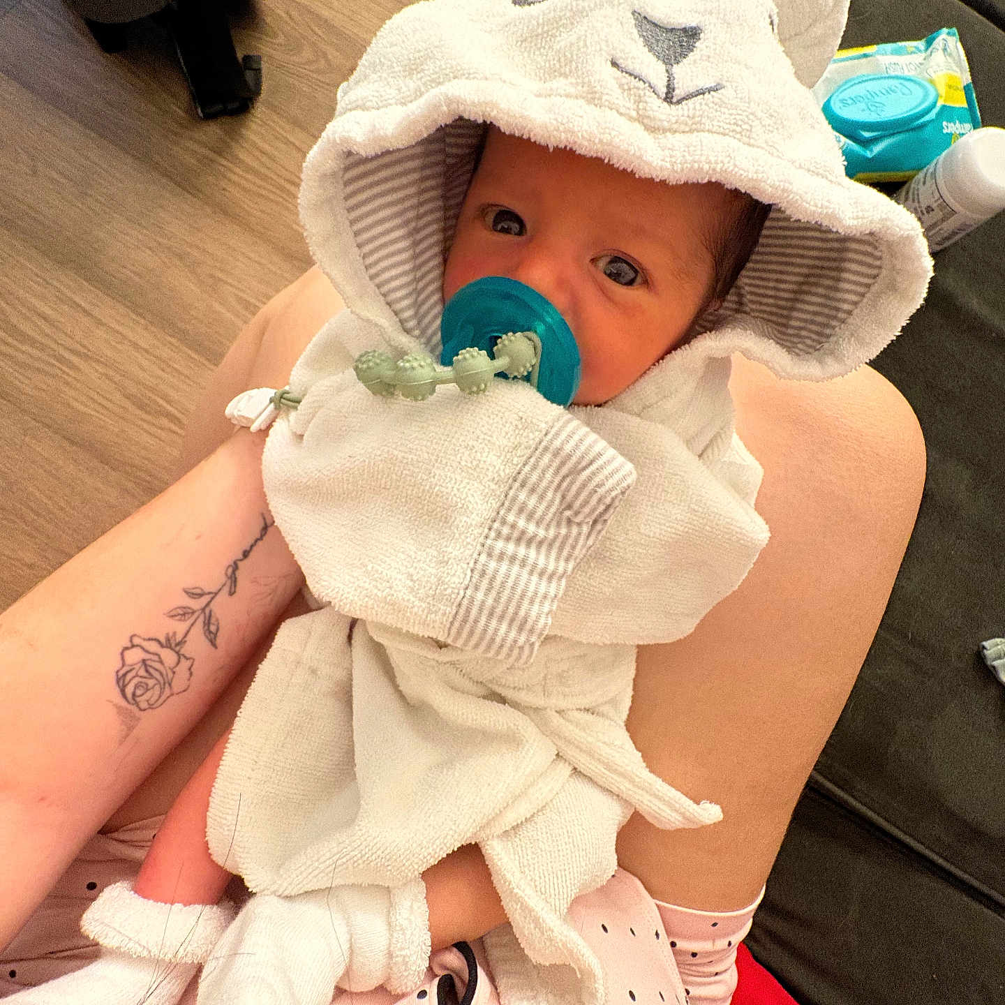 Davier is registered to the contest to win money with this photo: baby, infant, child, portrait, pacifier, hooded_outfit, animal_hood, blanket, towel, plush_toy, toy, couch, adult, holding, tattoo, indoor, home, sitting, pink_clothing, cozy