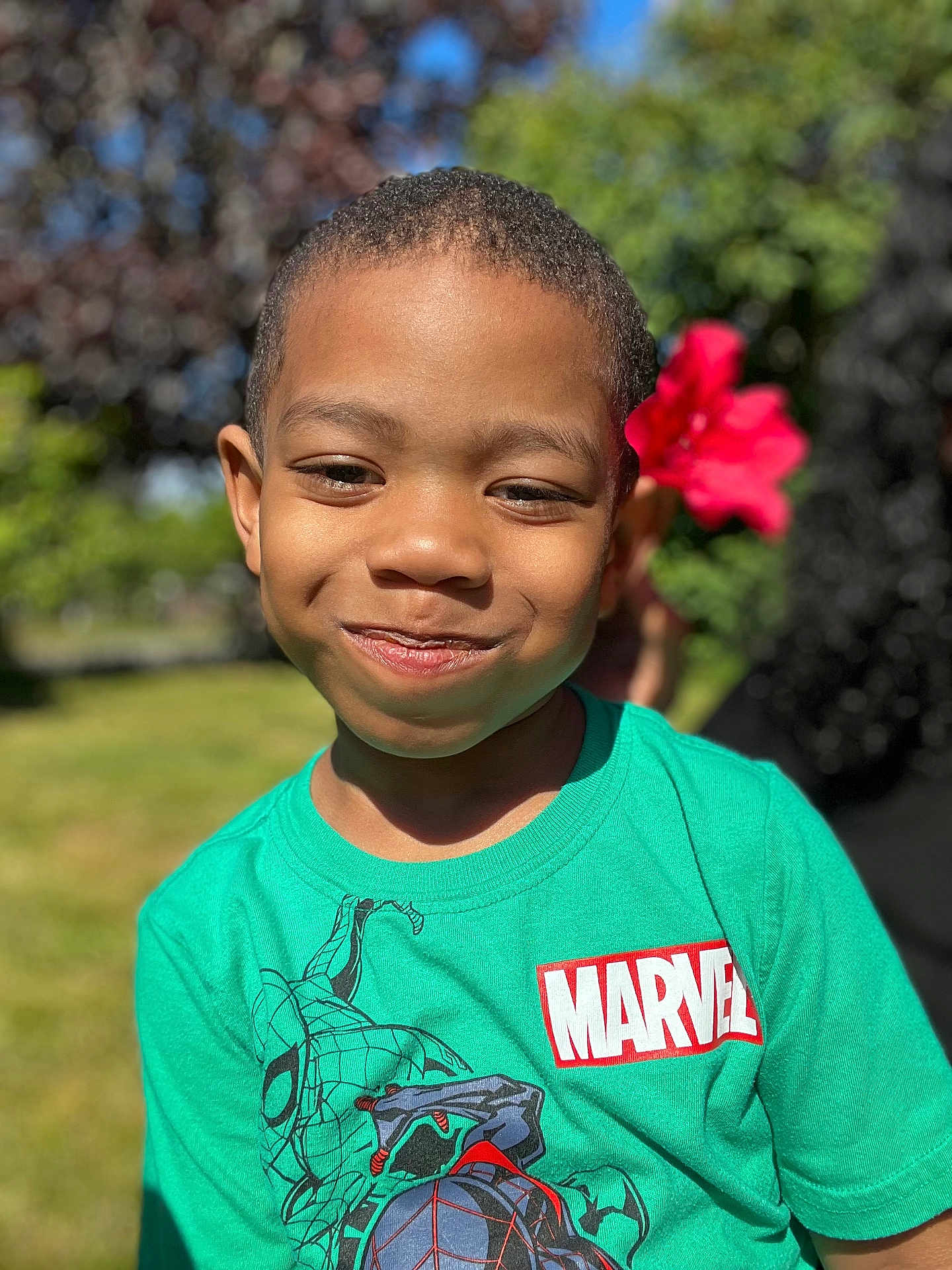 Kenji joined the competition — help win amazing prizes! child, boy, smile, face, green_tshirt, marvel_logo, flower, outdoor, nature, sunlight, grass, tree, happy, portrait, casual_clothing, short_hair, daylight, person, cute, playful