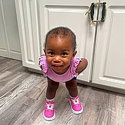 Koila joined the competition — help win amazing prizes! toddler, child, smiling, indoor, floor, wood_floor, pink_shoes, purple_top, curly_hair, kitchen, cabinet, playful, young_child, standing, person, sneakers, happy, cute, looking_up, casual_clothing