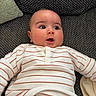 baby, infant, face, expression, striped_clothing, couch, pillow, texture, curious, surprised, laying_down, indoor, child, person, closeup, casual_wear, home, soft_lighting, cozy, young