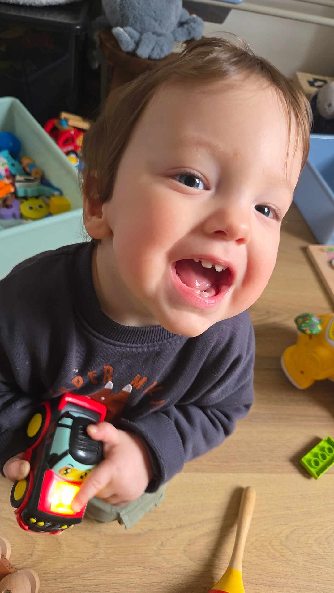 Alex a rejoint le concours — aidez-le/la à gagner de superbes lots ! child, toddler, smiling, toys, toy_car, indoor, playroom, wooden_floor, close_up, portrait, happy, teeth, hand, clothing, cheeks, mouth_open, sitting, daylight, young_child, play