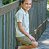 boardwalk, boy, casual, child, daylight, footwear, greenery, happy, leaning, nature, outdoor, person, playful, portrait, shirt, shorts, smiling, summer, wood, wooden_fence