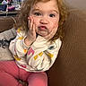 Oakley is registered to the contest to win money with this photo: child, toddler, curly_hair, pink_pants, sweatshirt, heart_pattern, couch, indoor, expression, funny_face, hands_on_face, cozy, person, home, water_bottle, table, blanket, casual_clothing, cute, portrait