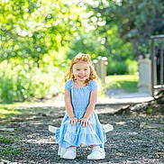 Oakley joined the competition — help win amazing prizes! child, girl, blue_dress, smiling, outdoor, sunlight, greenery, gravel_path, chair, happy, portrait, nature, daylight, small_chair, young_child, curly_hair, casual_clothing, cute, sitting, playful
