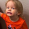 toddler, child, orange_shirt, black_cat, bat, halloween, playful, portrait, indoor, curly_hair, expression, wall, texture, casual_clothing, person, cute, fun, smile, young_child, bright_colors