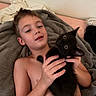 child, kitten, cat, black_cat, pet, animal, bed, blanket, bedroom, portrait, lying_down, holding, hands, face, eyes, indoor, cozy, cuddling, playful, photography