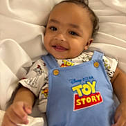 Silas is registered to the contest to win money with this photo: toddler, child, baby, smile, toy_story, clothing, blue_overall, blanket, cute, happy, portrait, infant, person, cute_face, soft_background, lying_down, indoor, young_child, button, fabric
