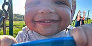 Silas is registered to the contest to win money with this photo: child, toddler, smiling, face, swing, playground, sunlight, outdoor, happy, grass, blue, hand, daylight, fun, park, baby, joy, person, nature, playing