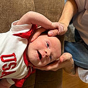 Sydney joined the competition — help win amazing prizes! baby, infant, child, smile, happy, hand, thumb, couch, brown_couch, white_shirt, red_shirt, usa, person, skin, face, expression, indoor, holding, relaxing, human