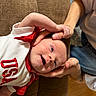 baby, infant, child, smile, happy, hand, thumb, couch, brown_couch, white_shirt, red_shirt, usa, person, skin, face, expression, indoor, holding, relaxing, human