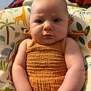 Annaleise is registered to the contest to win money with this photo: animal_print, arms, baby, child, closeup, comfort, cushion, cute, expression, face, home, indoor, infant, orange_dress, person, portrait, seated, serious, skin, young_child