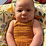 animal_print, arms, baby, child, closeup, comfort, cushion, cute, expression, face, home, indoor, infant, orange_dress, person, portrait, seated, serious, skin, young_child