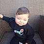 baby, child, smile, black_clothing, nike_logo, sweater, giraffe_toy, woven_chair, outdoor, sunlight, happy, cute, infant, playful, sitting, toy, person, portrait, casual, cozy