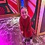 Emily is registered to the contest to win money with this photo: background, boots, child, decorations, face, festive, floor, girl, happy, holiday, indoor, lighting, person, playful, red_dress, smiling, snow, standing, winter_theme, wood_floor