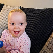 Layla is registered to the contest to win money with this photo: baby, smile, pink_clothing, bottle, couch, pillow, indoor, child, happy, portrait, seated, young_child, face, hand, cozy, home, cute, infant, expression, comfort