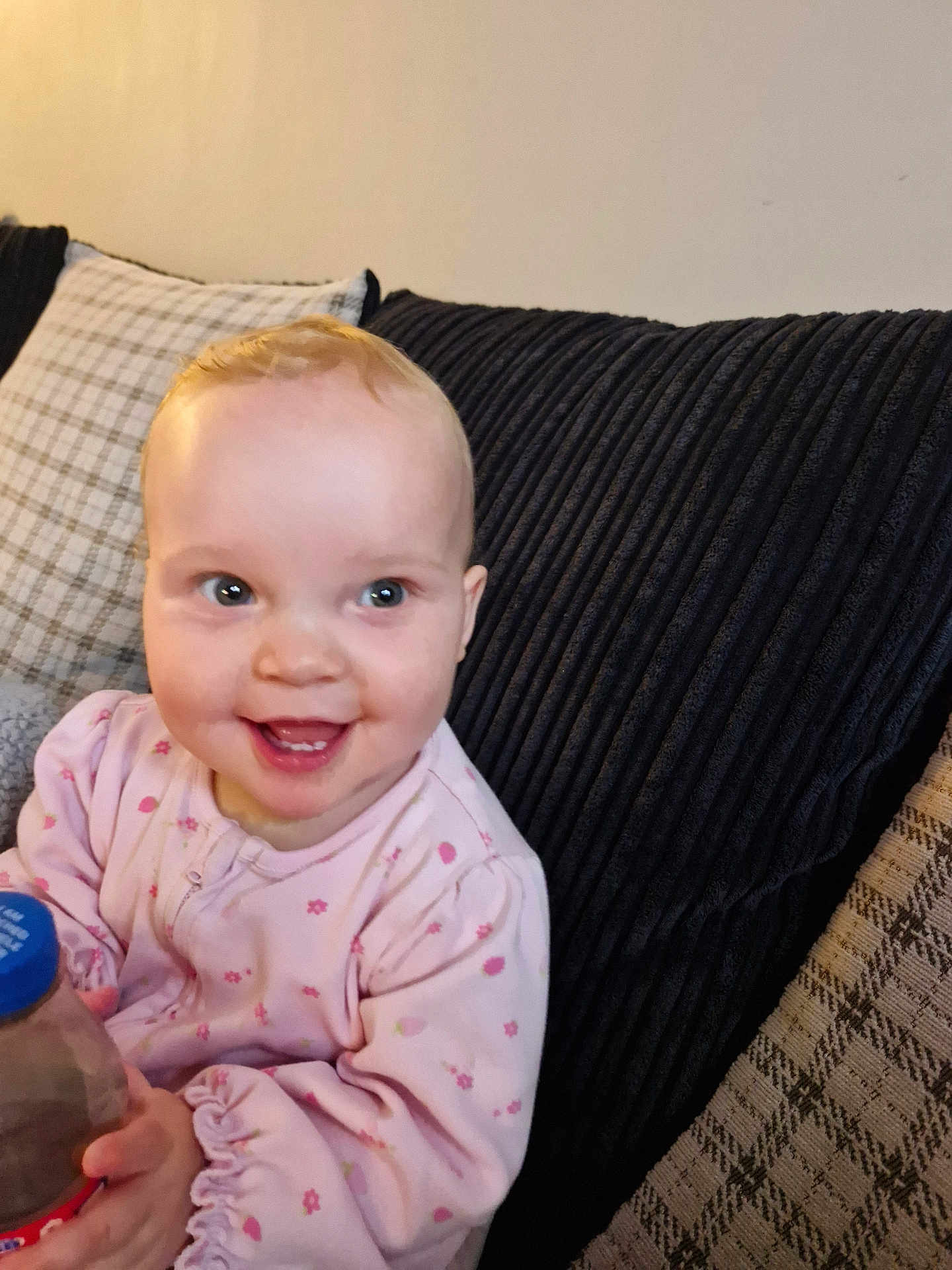 Layla is registered to the contest to win money with this photo: baby, smile, pink_clothing, bottle, couch, pillow, indoor, child, happy, portrait, seated, young_child, face, hand, cozy, home, cute, infant, expression, comfort