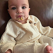 Ava is registered to the contest to win money with this photo: baby, child, infant, knitwear, cream_color, sweater, pants, couch, leather, food, face, hand, foot, cute, indoors, portrait, young, cozy, relaxing, casual