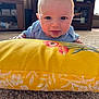 Soulstyn is registered to the contest to win money with this photo: baby, infant, smiling, blue_clothing, yellow_pillow, floral_pattern, carpet, indoor, living_room, furniture, cabinet, natural_light, cute, face, head, person, playful, happy, toddler, home