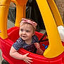 toddler, child, toy_car, red, yellow, headband, pink, smile, outdoor, deck, play, cute, happy, person, plastic, small_wheels, blue_button, short_sleeve, patterned_shirt, curly_hair