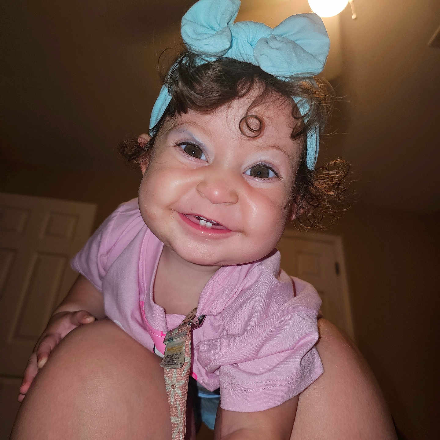 Ziora is registered to the contest to win money with this photo: baby, blue_headband, ceiling_light, child, closeup, curly_hair, cute, face, happy, headband, human, indoor, knees, person, pink_shirt, playful, portrait, room, smiling, toddler