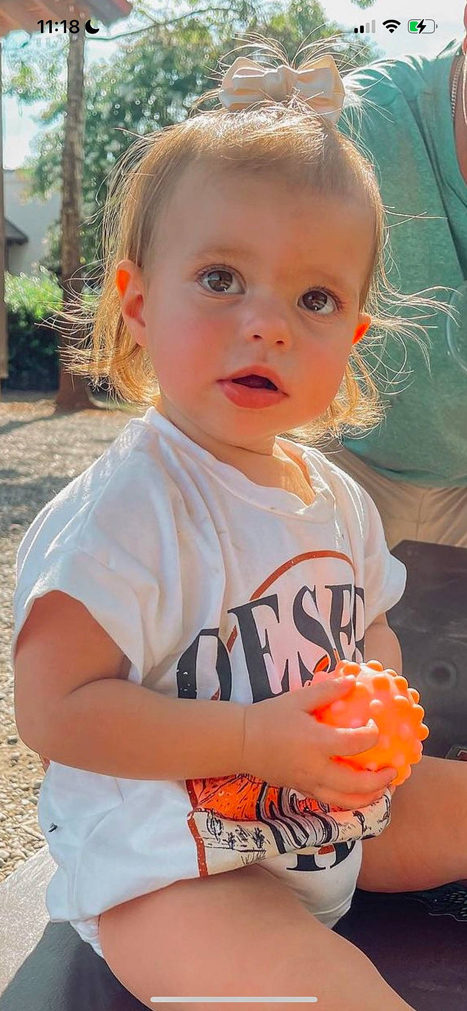 Vera is registered to the contest to win money with this photo: arm, baby, baby_toddler_clothing, cheek, child, eye, fun, happy, head, iris, mouth, nose, orange, people, person, plant, skin, sleeve, summer, t_shirt